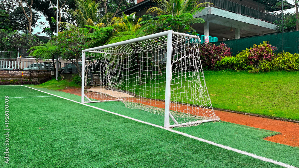 Fototapeta premium A soccer goal is on a field with green grass. The goal is white and has a net