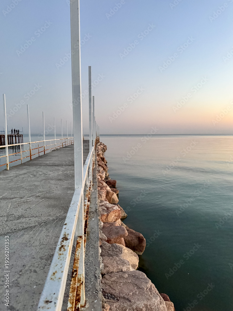 Fototapeta premium Pier at Issyk Kul Lake in Kyrgyzstan during calm evening. Minimal composition, smooth water surface and pastel sky tones.