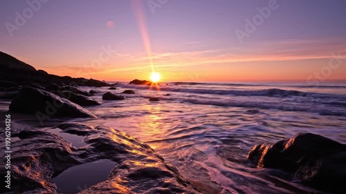 A vibrant sunset over a rocky coastline, with the sun's rays reflecting on the water