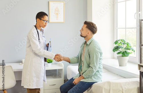 Fotografi Clinic room meeting, female doctor shaking hands with male patient sitting on ex