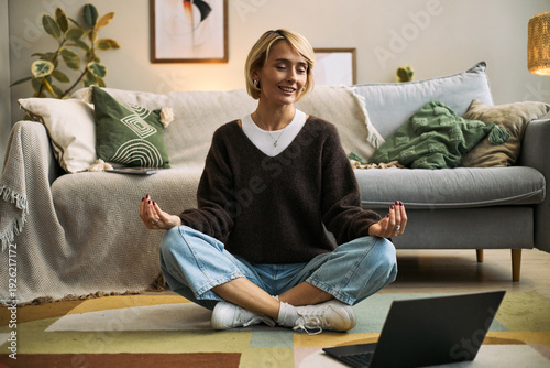 Φωτογραφία Caucasian woman sitting cross legged on floor meditating in front of open laptop