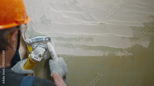 Construction worker sanding interior wall with power tool