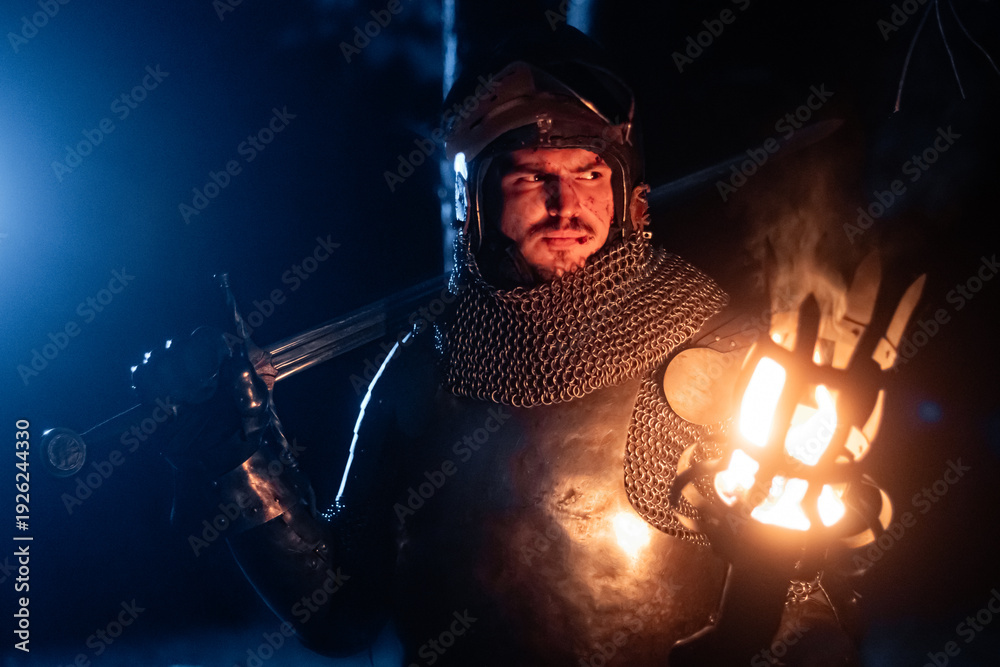 Obraz premium A knight in full armor, sword and torch in hand, walks through a gloomy night forest. A medieval warrior, bloodied and scarred, hunts and searches in the darkness.