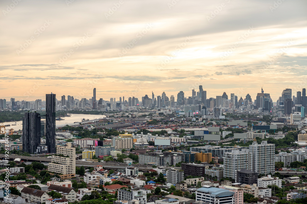 Obraz premium Expansive urban skyline with dense high-rises and a winding river under a cloudy evening sky, showcasing a sprawling modern cityscape. Bangkok, Thailand