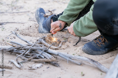 Bushcraft expert starting campfire with fire starter on sand