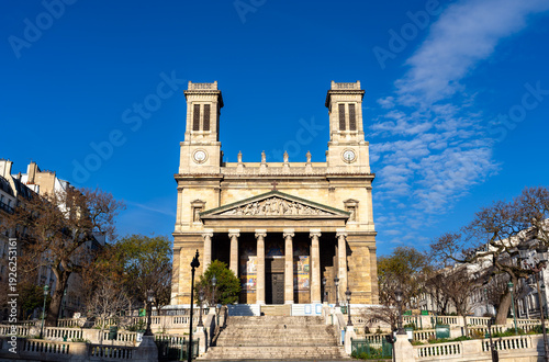 Scenic sunny view of the symmetrical neoclassical architecture, twin towers, and wide stone stairs of the Saint-Vincent-de-Paul church in the 10th arrondissement of Paris, France.