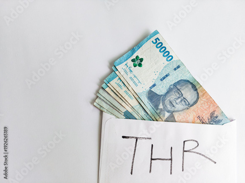 Obraz na płótnie An envelope labeled as THR contains stacked Indonesian Rupiah banknotes, isolated on white background, symbolizing mandatory Eid holiday allowance for workers as yearly incentive in Indonesia
