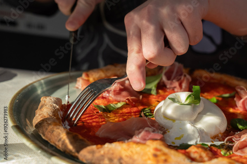 dłonie osoby krojącej kawałek pizzy