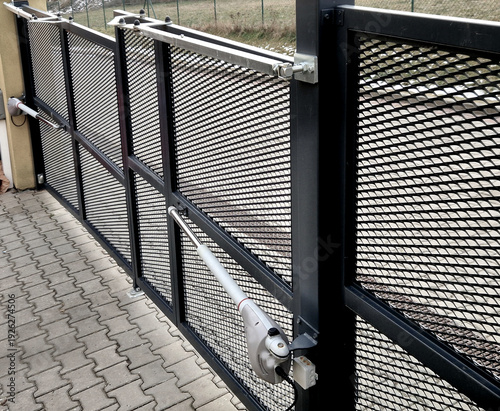 Two-wing entrance gate with expanded metal filling. Expanded metal filling transparency. Drives with electric piston drives that allow automatic opening using a remote control. drive way