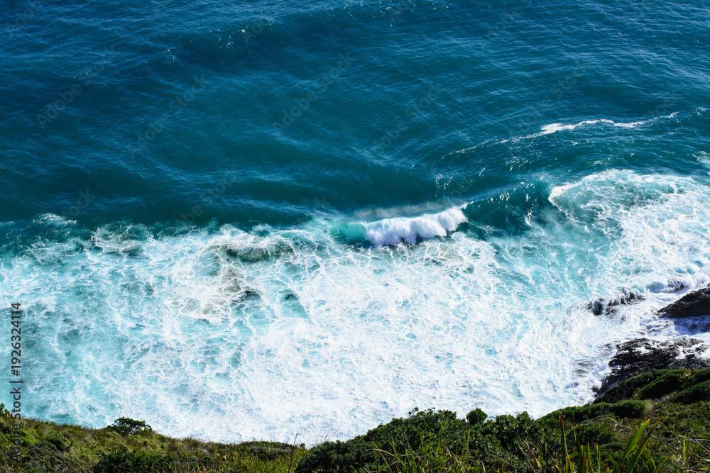 Obraz premium Aerial view of a giant ocean wave crushing onto the shore. Top down photo of turquoise sea water surface. White foam waves texture as natural background