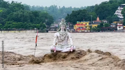 Close-up of a river overflowing as a result of flooding, reaching a statue of Shiva in India.