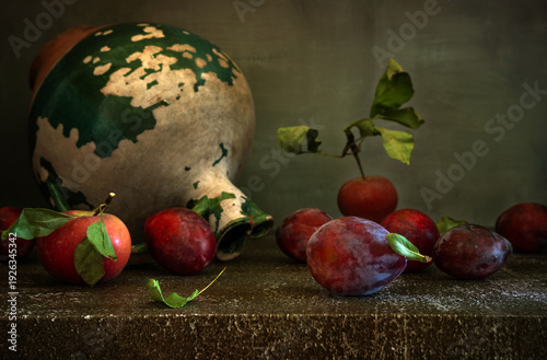 Still life with ripe and delicious plums, an apple and an old ceramic jug.