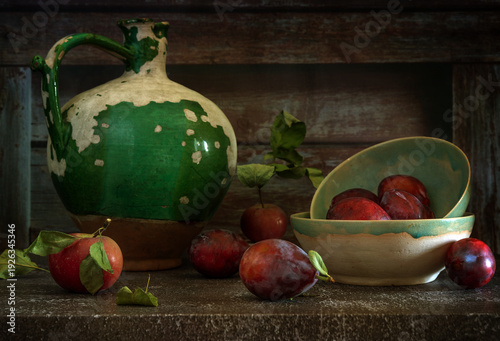 Still life with ripe and delicious plums, an apple and an old ceramic jug.