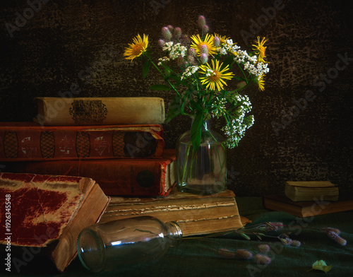 A small bouquet of meadow flowers and old books on a dark background.