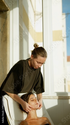 Black client receiving facial from white aesthetician on sunlit balcony