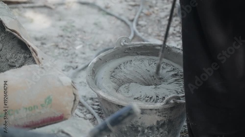 Construction worker mixing cement mortar in metal bucket at building site. Masonry preparation, renovation process and industrial material concept.