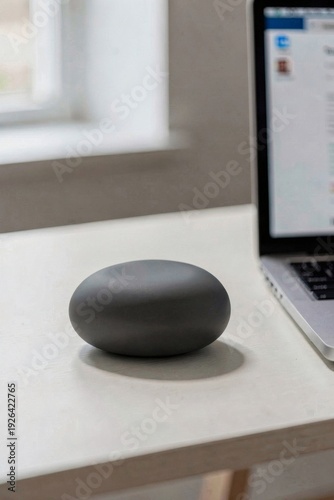 Minimalist charcoal noise machine shaped like a pebble on desk