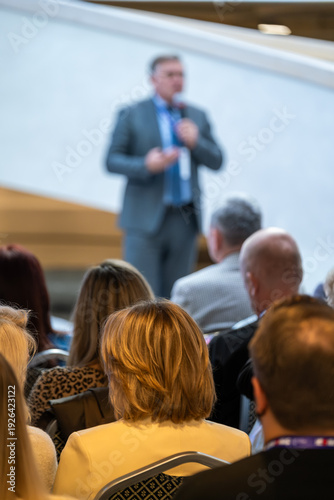Wallpaper Mural Speaker presents at conference, captivating professionals in audience. Formal setting with blurred attendees. Focus on message, leadership, business growth. Engaging talk fosters networking, ideas. Torontodigital.ca