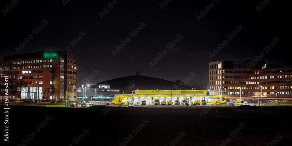 Fototapeta premium Dutch business district at night with delivery van depot dome-shaped arena and illuminated office buildings viewed from across dark field