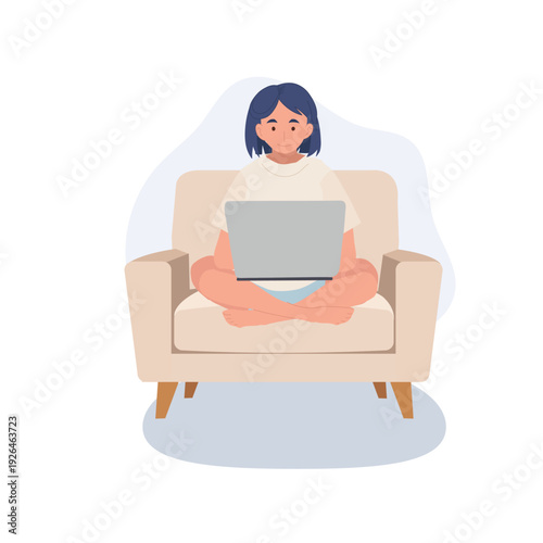 young woman using laptop indoors remote work and online learning. female freelancer sitting cross legged on armchair with computer