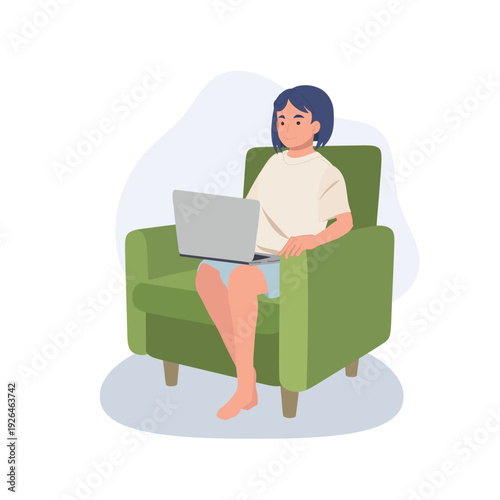 Young woman working on a laptop at home, sitting comfortably in a green armchair in the living room during daytime,