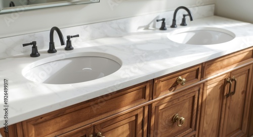 Two sinks with black water taps on polished white countertop over wooden bathroom vanities