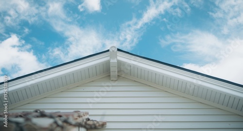 White fascia and soffit on a vinyl sided gable roof highlighted with corbel and bracket details set against sky scene