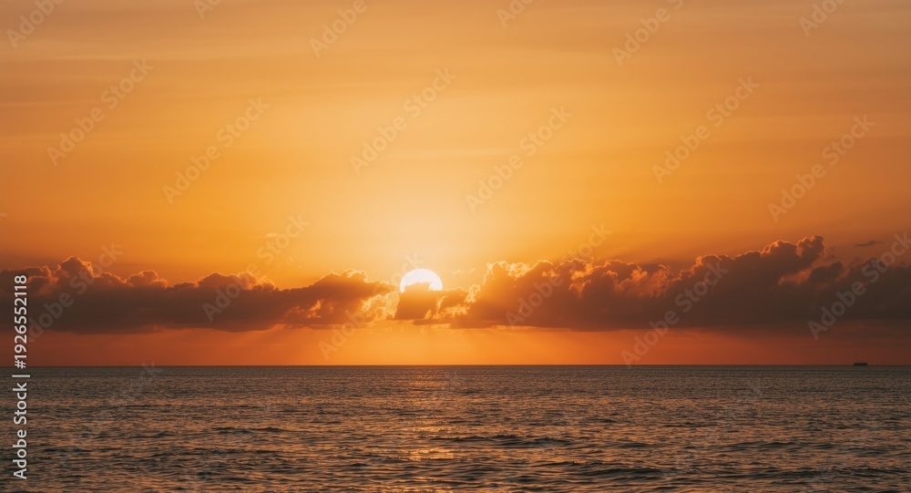 Obraz premium Sunset casting warm orange hues over calm sea and gentle white clouds