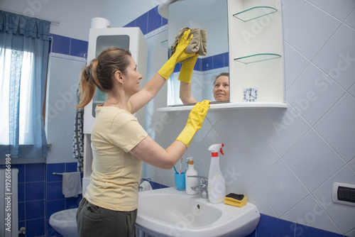 Fotografie Woman wearing yellow protective gloves and concentrating on carefully wiping and