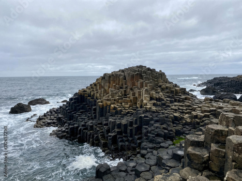 The Giant's Causeway, a natural wonder of hexagonal basalt columns on the coast of Northern Ireland, meeting the turbulent sea under a cloudy sky.
