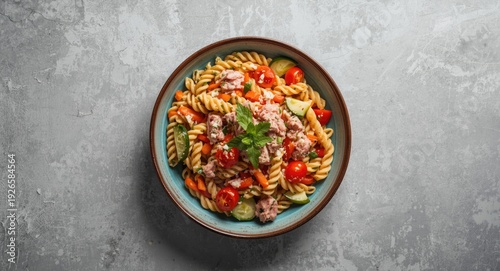 Colorful tuna pasta salad with fresh garden vegetables served in retro bowl on radiant concrete background overhead shot