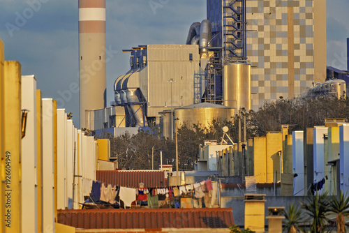 Thermal Power Plant near the Leirosa Beach landscape, its tall stacks releasing thin trails of smoke into a sky. Rows of yellow and white structures line the site,