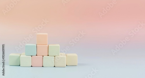 Pastel colored cubes piled in gradient hues on a soft pink and blue canvas background with copy space
