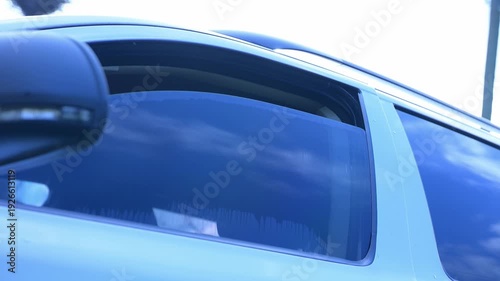 A serene view emerges from a car window, showcasing a bright blue sky dotted with clouds. Sunlight filters in, hinting at upcoming adventures and journeys. Raising up a car door window.