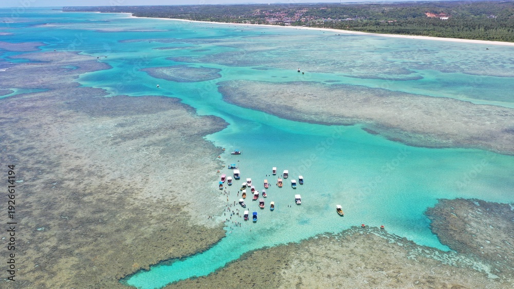 Obraz premium Fantastic aerial view of the turquoise waters of Toque beach with dozen of small boats with tourists on the natural pools formed among coral reefs in Milagres route near Maceio, Alagoas State, Brazil