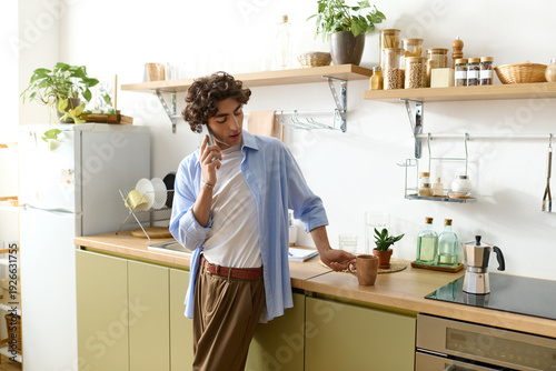 Fényképezés Curly-haired young man enjoys a relaxing moment at home in his vibrant kitchen