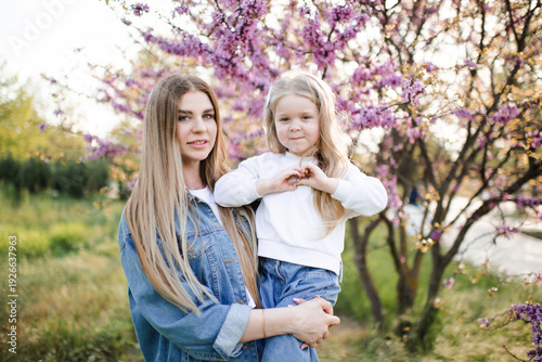 Mother having fun with child girl daughter 4-5 year old in park with blooming tree in sunny day. Motherhood. Springtime.