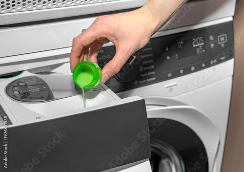 Obraz na płótnie Woman pouring liquid detergent from green cap into washing machine drawer