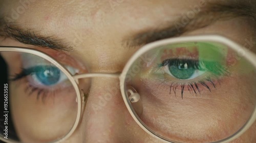 Intense close up woman eyes in glasses looking at screen, with reflections of colorful data charts, graphs on lenses, indicating focus on analytics, digital work. Woman eyes looking at computer screen