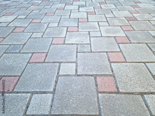 A close-up of a paved road made of patterned stone with gray and reddish blocks arranged in a geometric pattern. The surface appears clean and well-maintained.