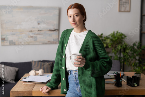 Cuadro en lienzo Young woman with red hair relaxes in her modern apartment sipping a warm drink
