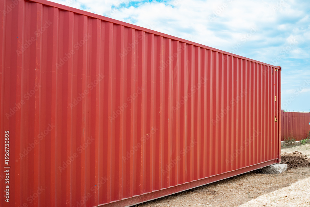 Fototapeta premium Side view of a long red corrugated shipping container on an outdoor storage site. international logistics, industrial transport, cargo storage.