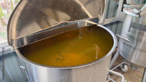 Stainless steel mixing tank with golden oil liquid in production line.