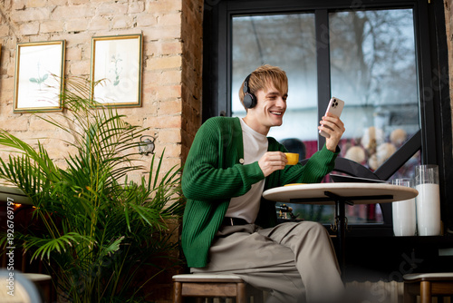 Cuadro en lienzo Smiling young man enjoying coffee and music in a trendy cafe setting