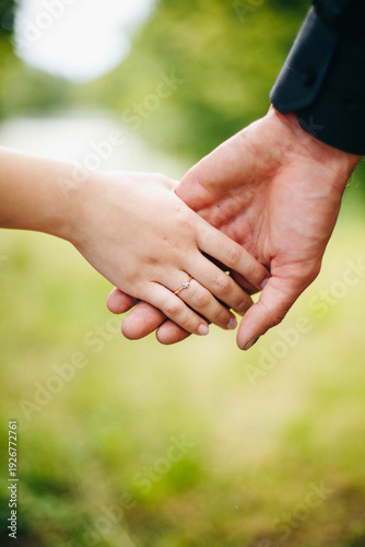 Close up of couple holding hands with engagement ring on woman’s finger. Romantic moment outdoors with soft green background, symbol of love, commitment and marriage proposal.