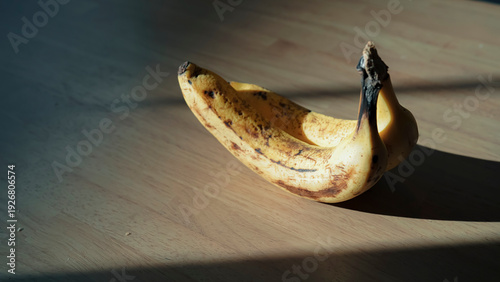 Photos 木目のテーブルに置かれたバナナ 差し込む自然光とドラマチックな影 静物 / Ripe bananas on wooden table with dramatic
