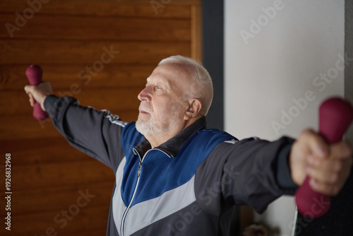 Elderly man exercises with dumbbells in a room during daylight hours for strength training and fitness