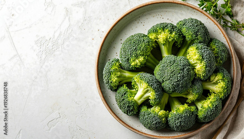 Fresh green broccoli florets in a ceramic bowl on a white textured background. Top view flat lay with copy space. Healthy organic raw vegetable food concept.