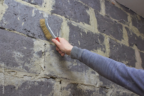 Removing mortar residue from wall, man with a metal brush cleans a wall, Preparing a wall for repair
