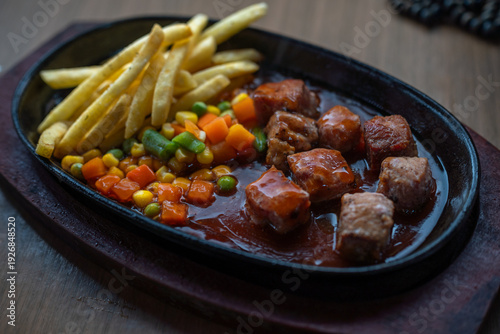 Photography Cubed meat in brown sauce with fries and mixed vegetables on hot plate